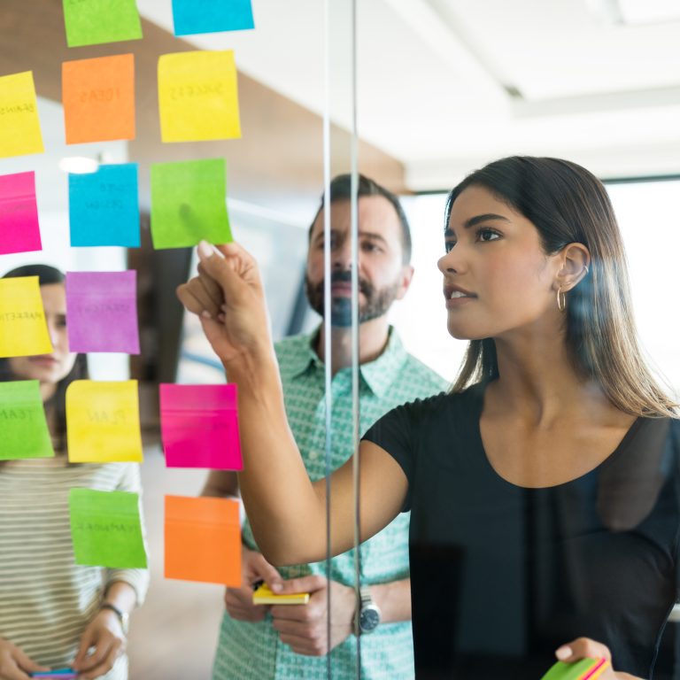 Female young manager discussing over adhesive note with coworkers in office meeting